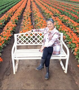 Photo of Julie on a white bench in front of colorful rows of flowers